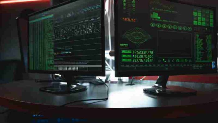 Close-up of dual computer monitors with green coding interfaces in a dark room, highlighting cyber security themes., tags: und - pexel